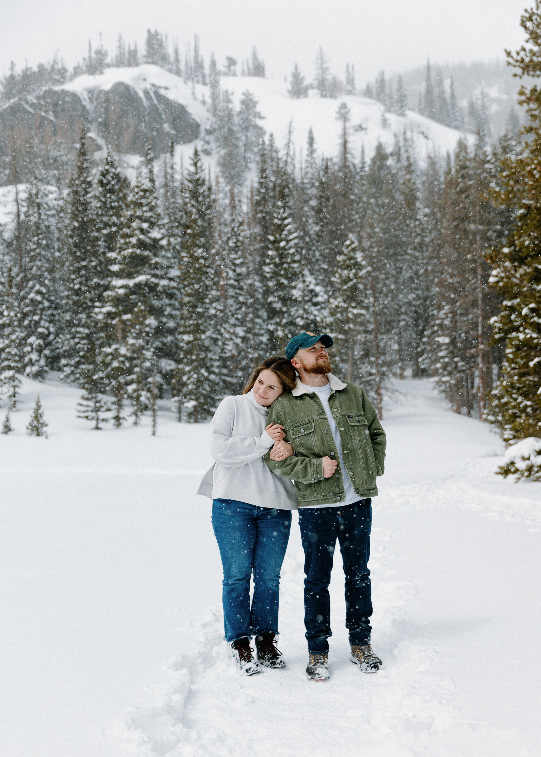 A loving couple embraces in a winter wonderland at Rocky Mountain National Park, surrounded by pristine snow-covered landscapes and majestic snow-capped peaks