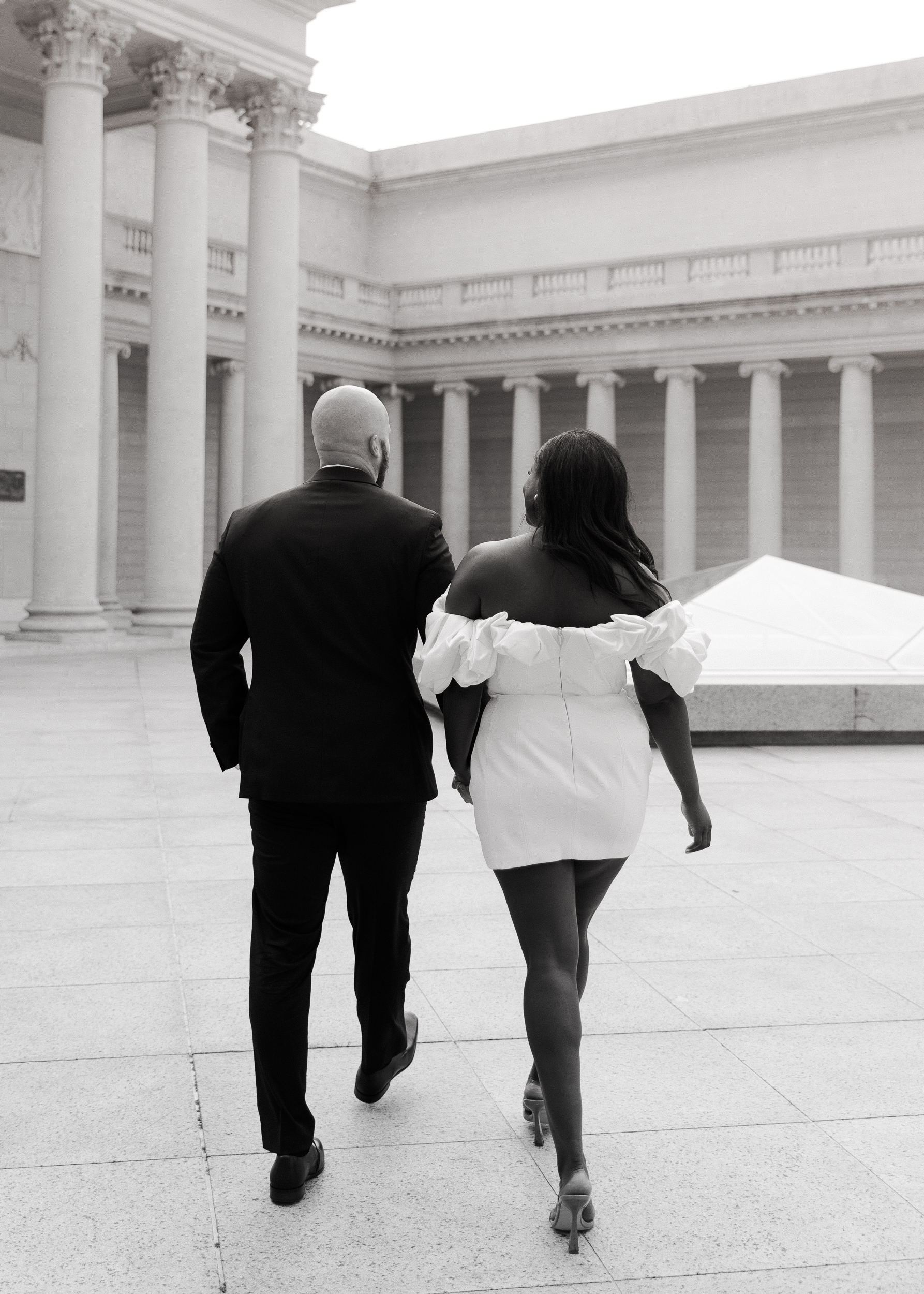 The couple walks hand in hand through the Legion of Honor's gardens, the fog casting an enchanting ambiance over the lush greenery and classical sculptures.