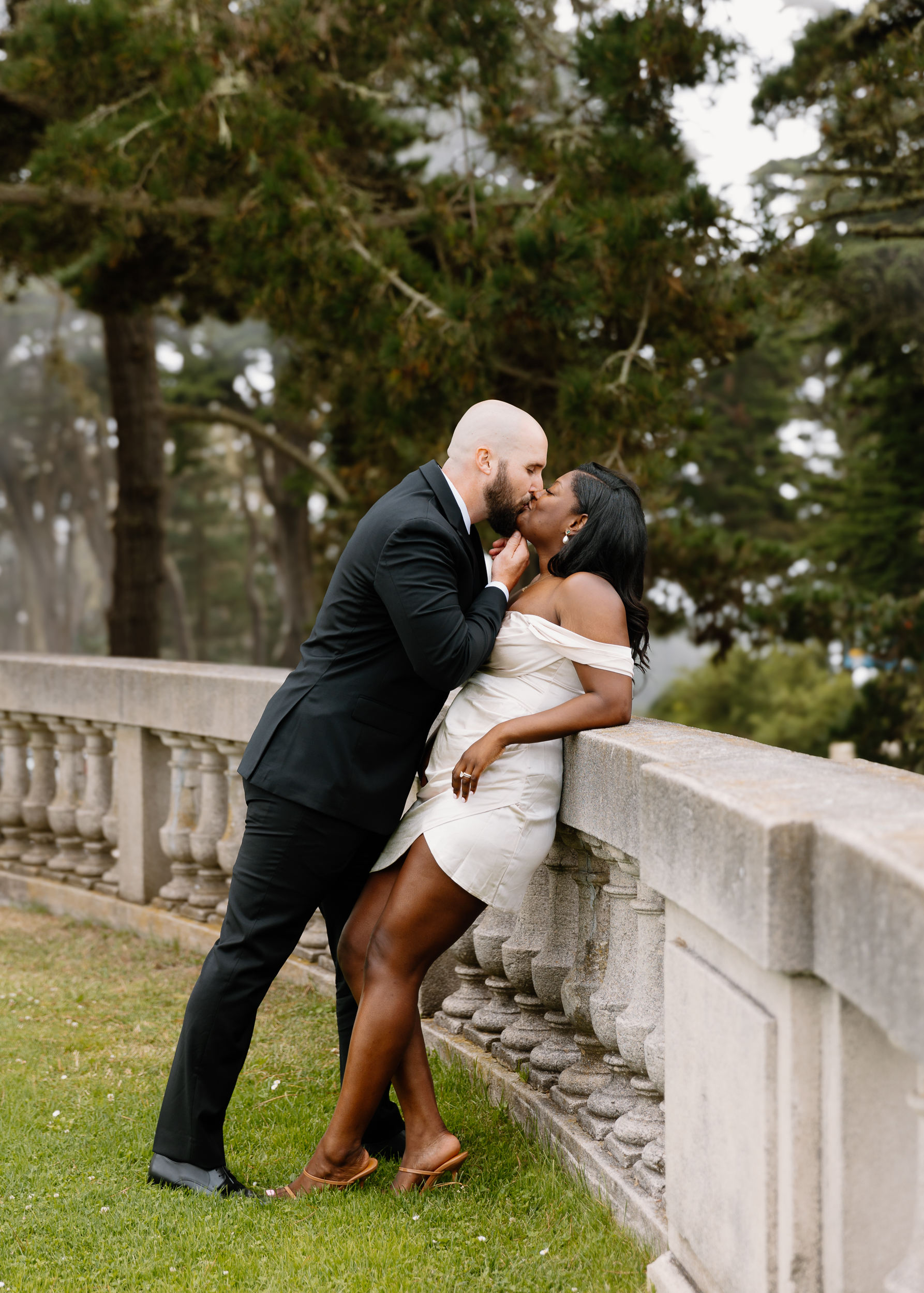 The couple shares a kiss, enveloped by the Legion of Honor's foggy allure, creating a romantic and timeless image.